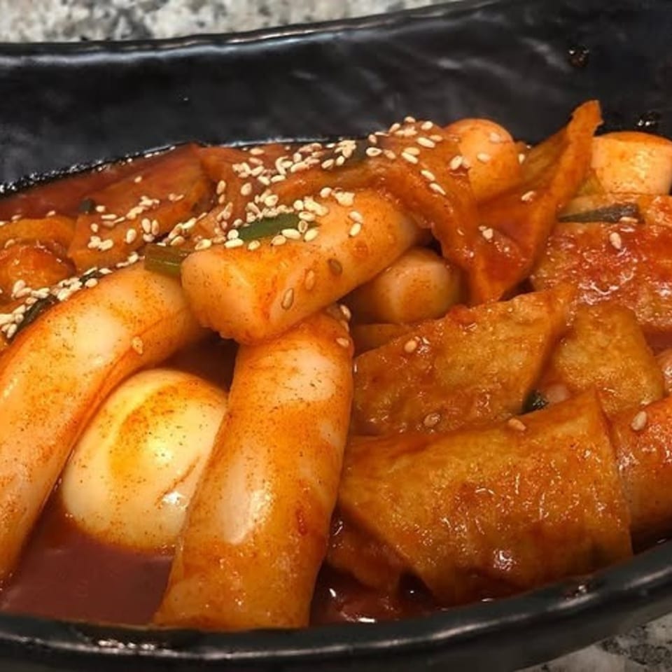 A close-up of Tteokbokki with rice cakes, fish cakes, and boiled eggs in a spicy red sauce.