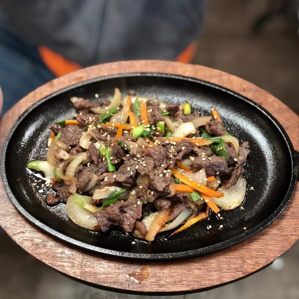 Sizzling Korean bulgogi with beef, onions, carrots, and green onions, topped with sesame seeds.