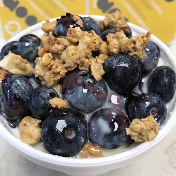 Close-up of blueberries and granola in a white bowl with milk, from The Koop.