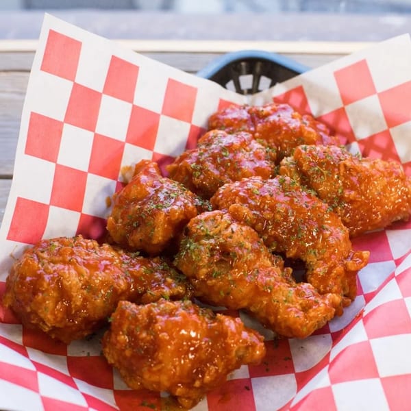 A basket of The Koop's Korean fried chicken wings, coated in a glossy red sauce and sprinkled with herbs.